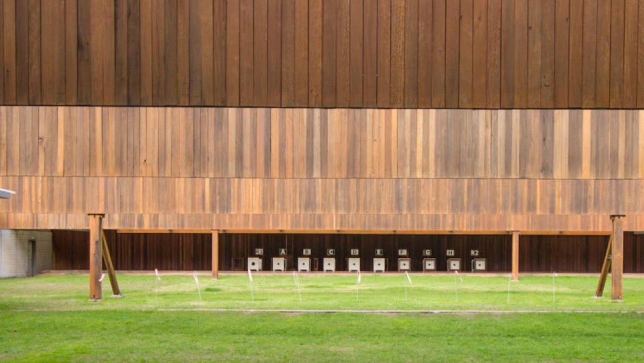 Shooting range with wooden wall, targets in stalls, and green grass in Brisbane.