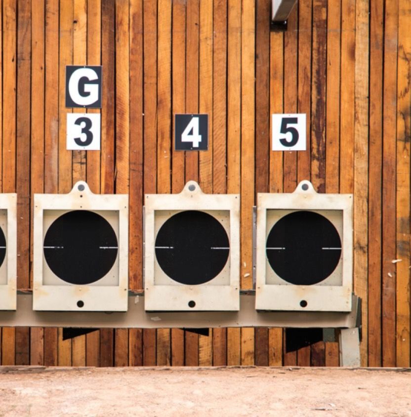 Three numbered shooting targets labeled G3, 4, and 5 mounted on a wooden wall at an outdoor range.