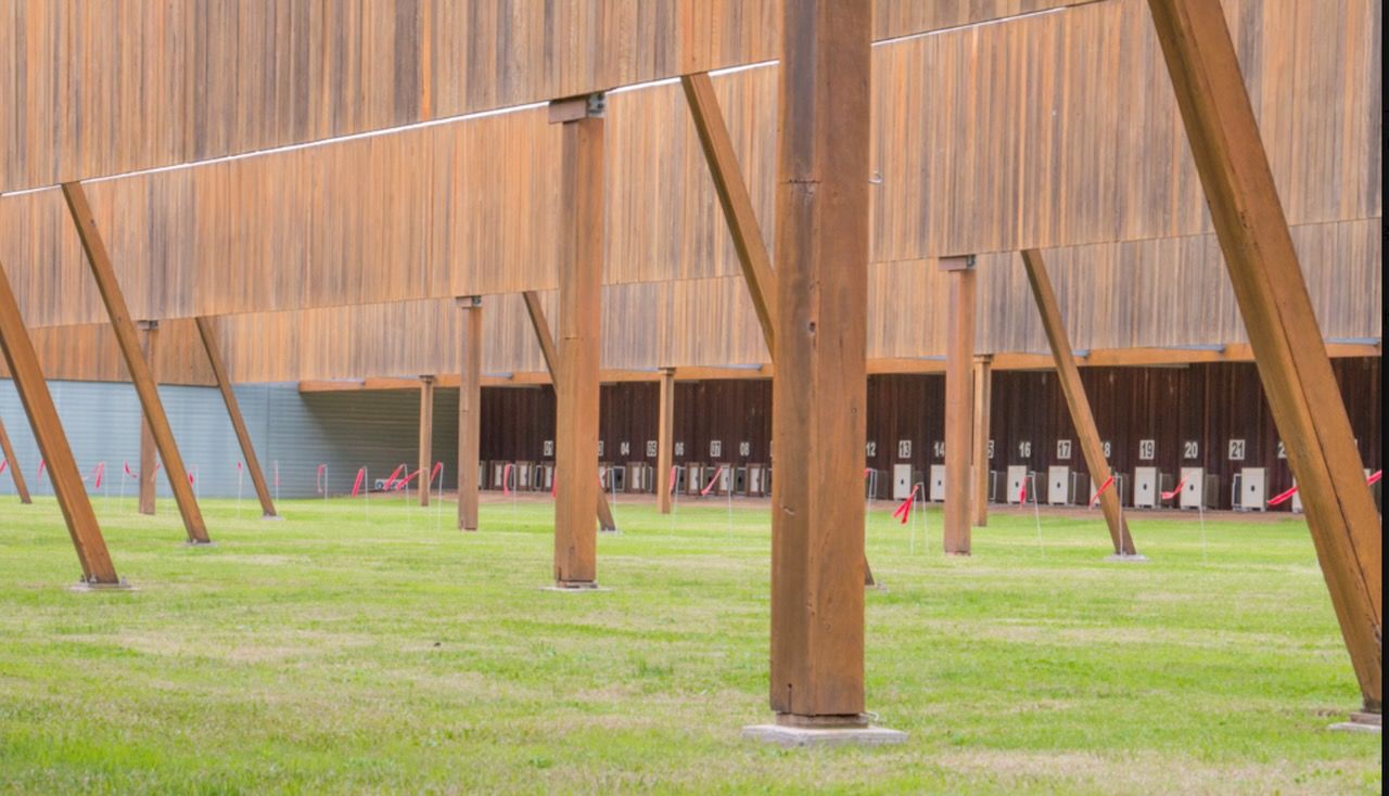 Brown wooden structure with supporting pillars on a grassy field; small red doors in the distance in Brisbane.