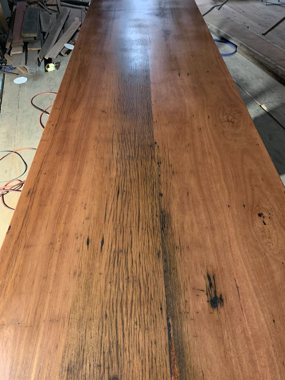 Long, finished wooden tabletop with varying reddish-brown tones and dark streaks, possibly timber.