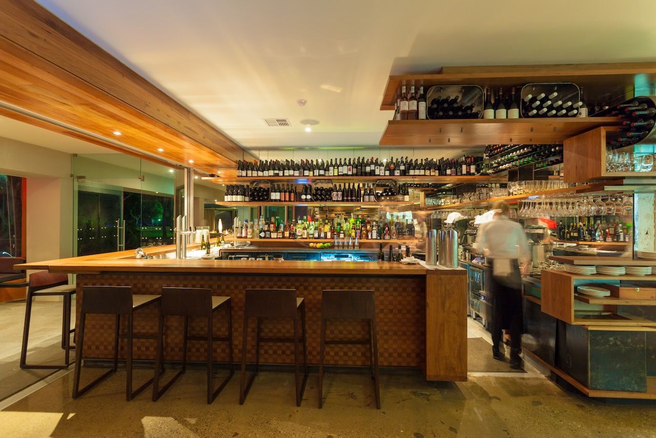 Bar with wooden decor, stocked shelves, and a bartender preparing drinks.