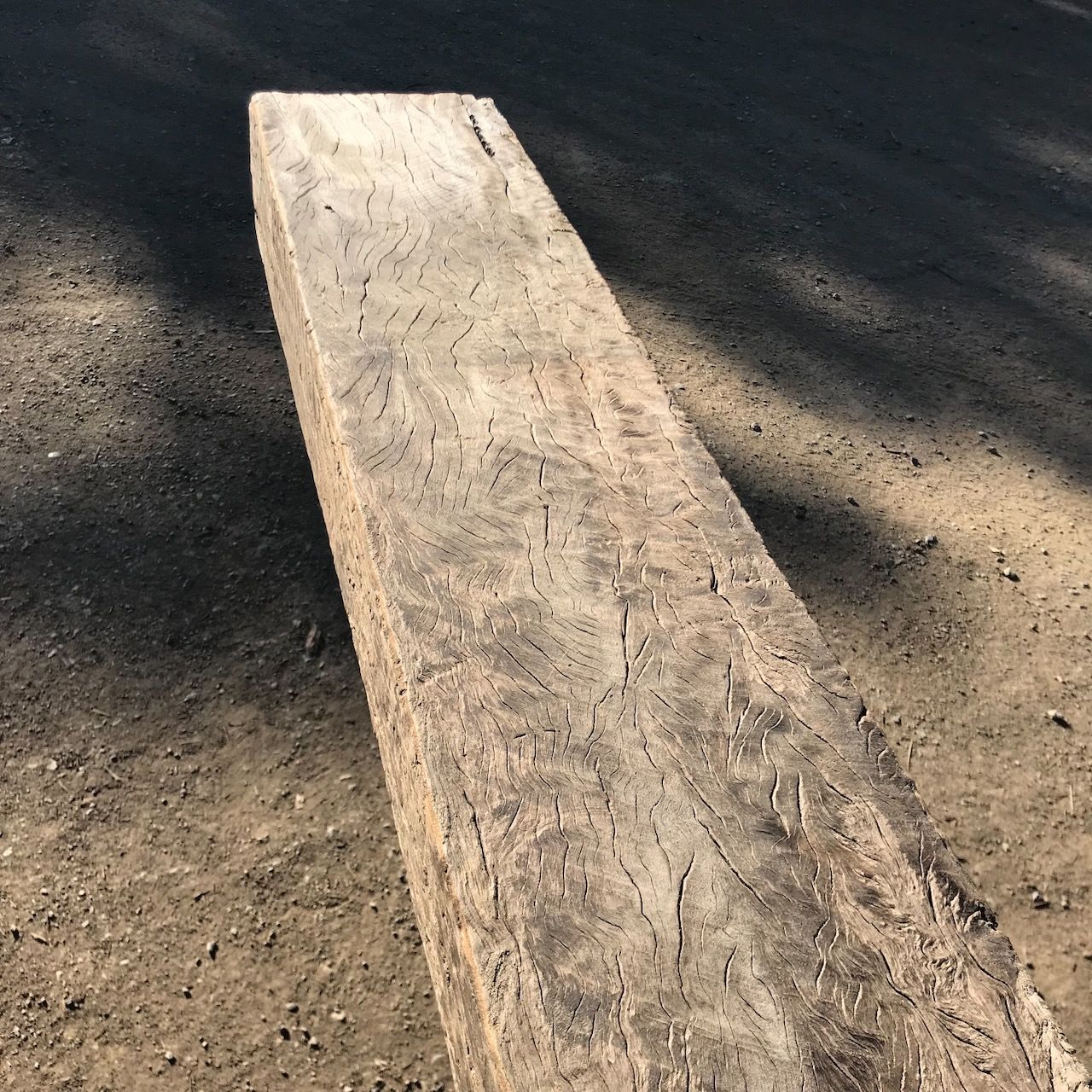 Weathered wooden beam resting on a dirt surface, with sunlight casting shadows.