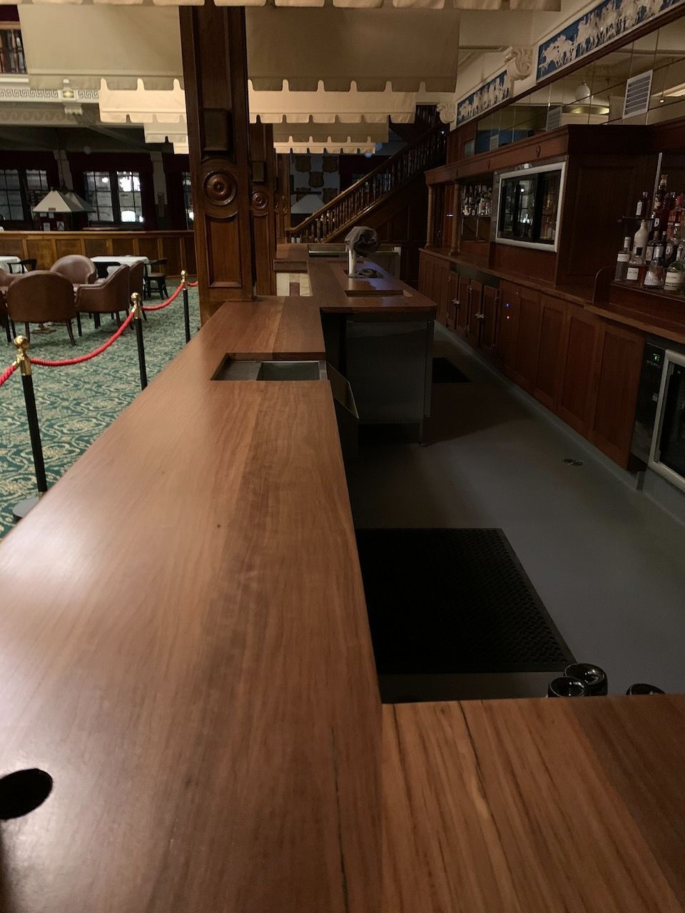 Empty wooden bar with cutouts, surrounded by dark wood decor and green carpet.