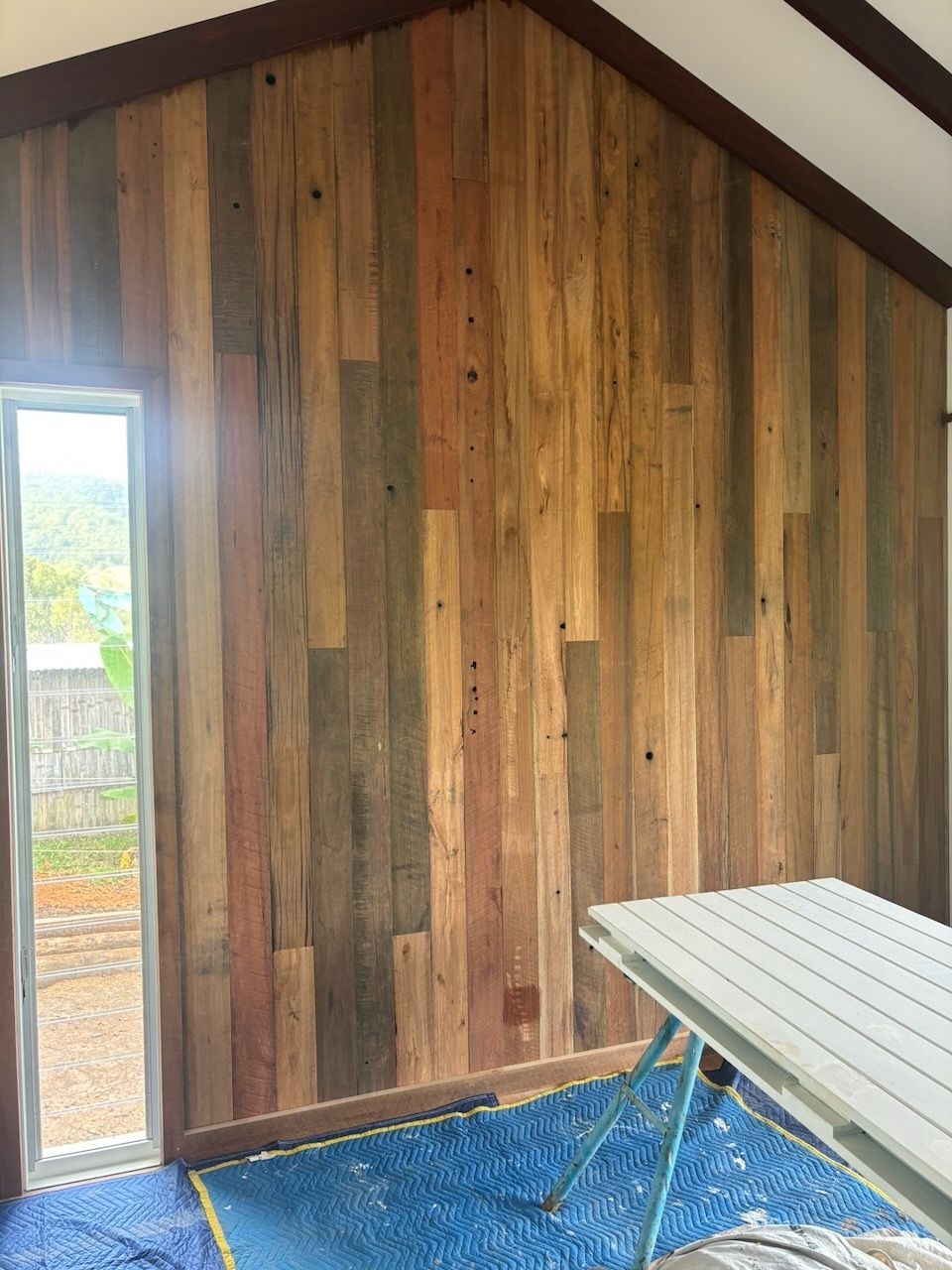 Interior with wood plank walls, door, and a folding table on a blue tarp in Brisbane.