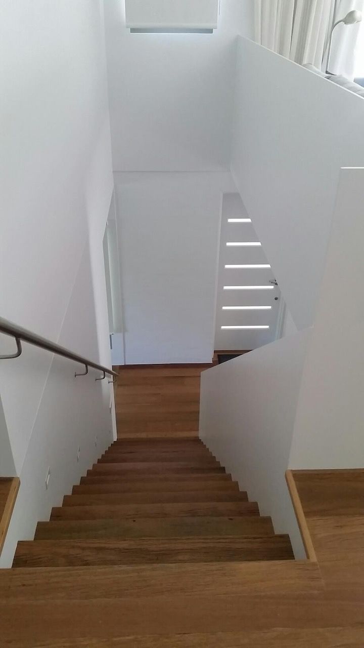 Wooden stairs leading down, enclosed by white walls and a metal handrail.