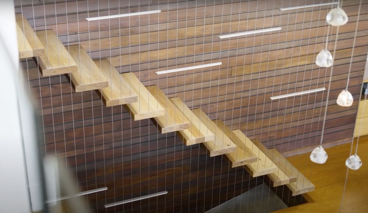Floating wooden staircase with metal cables against a wood paneled wall. Several hanging lights in Brisbane.