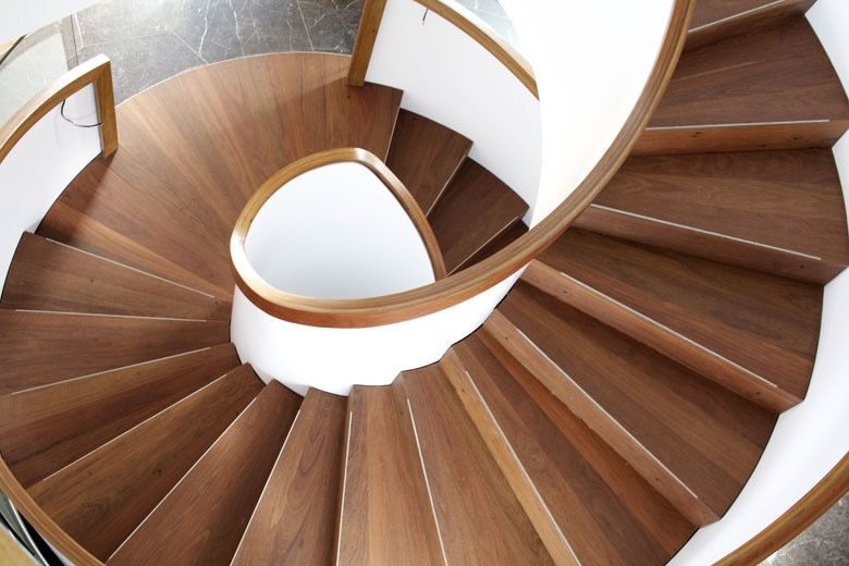 A high-angle view of a wooden spiral staircase with a white central support structure and matching wooden handrails.