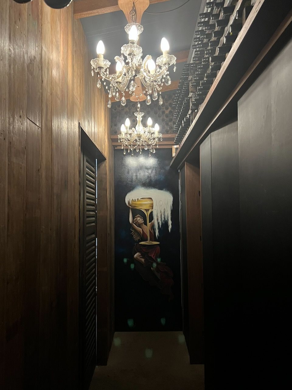 A dimly lit hallway with wood paneling, crystal chandeliers, and a mural of a glass of beer on the far wall.