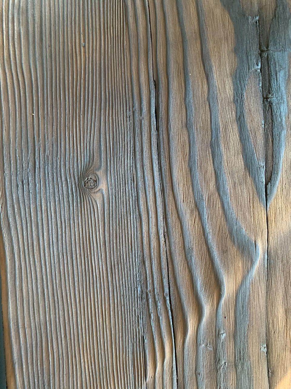 Close-up of weathered brown wood grain with vertical patterns, deep grooves, and a small knot.