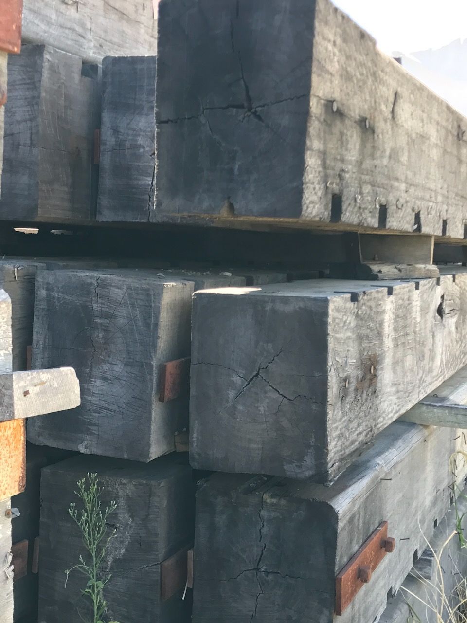 Pile of weathered, dark wooden beams with visible cracks and metal plates.