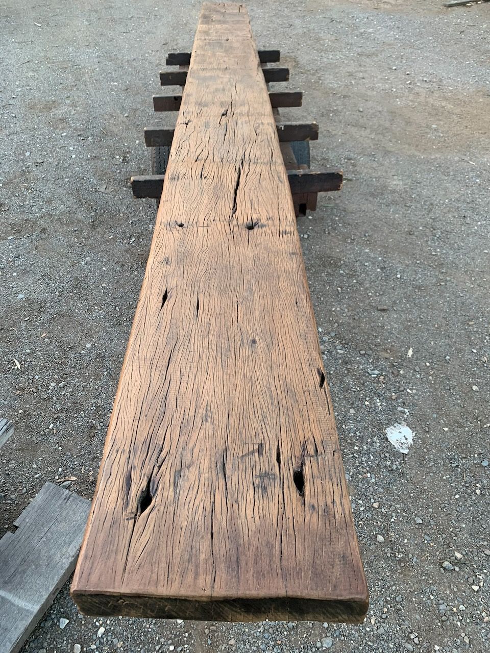 A long, weathered wooden beam resting on supports on a gravel surface.