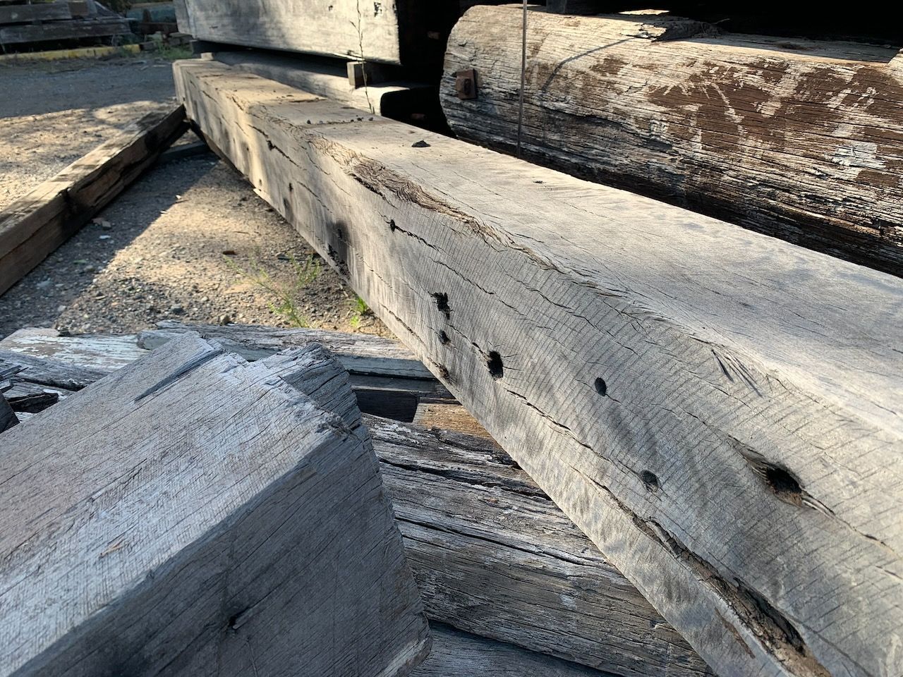 Gray, weathered wooden beams stacked outdoors, close-up with visible holes and knots.