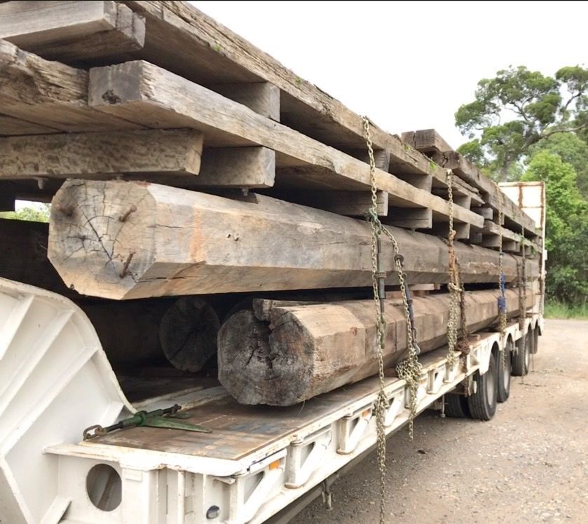 A flatbed truck loaded with large, weathered wooden beams, secured by chains, outdoors.