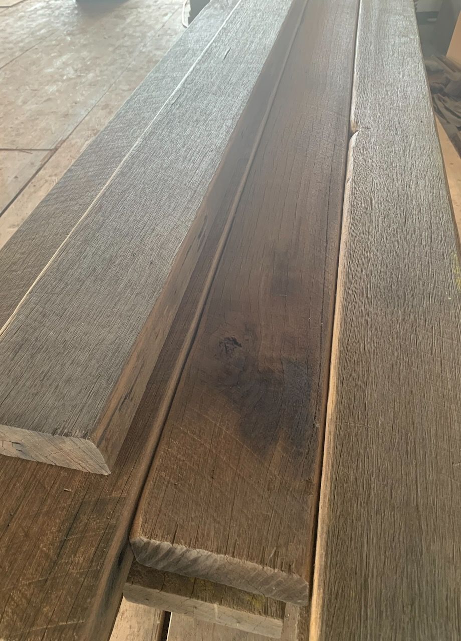 Three rough-sawn wooden boards lie parallel to each other on a workshop floor, showing varied brown and grey wood grains.