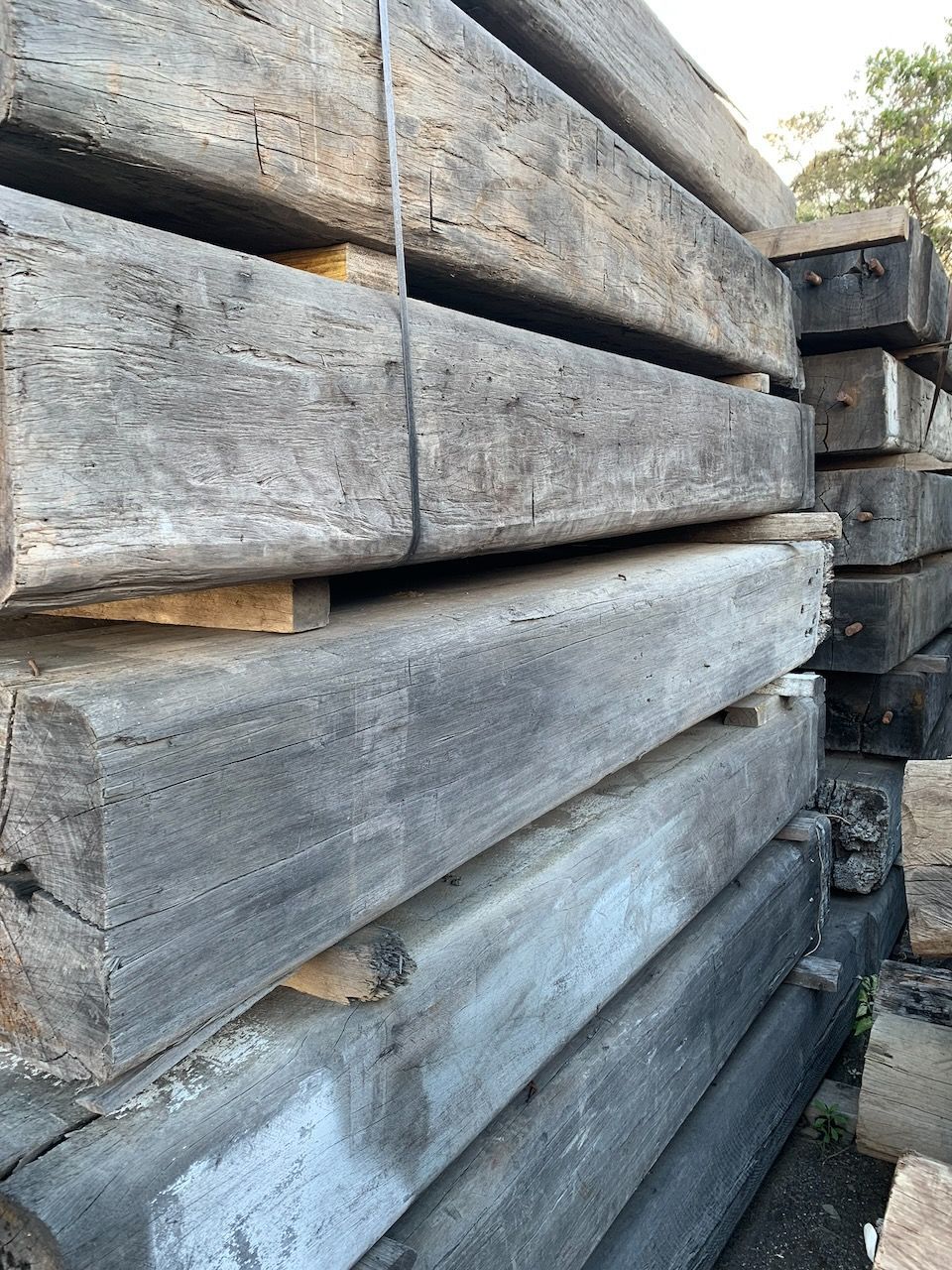 Pile of weathered, rectangular wooden railroad ties, stacked outdoors in Brisbane.