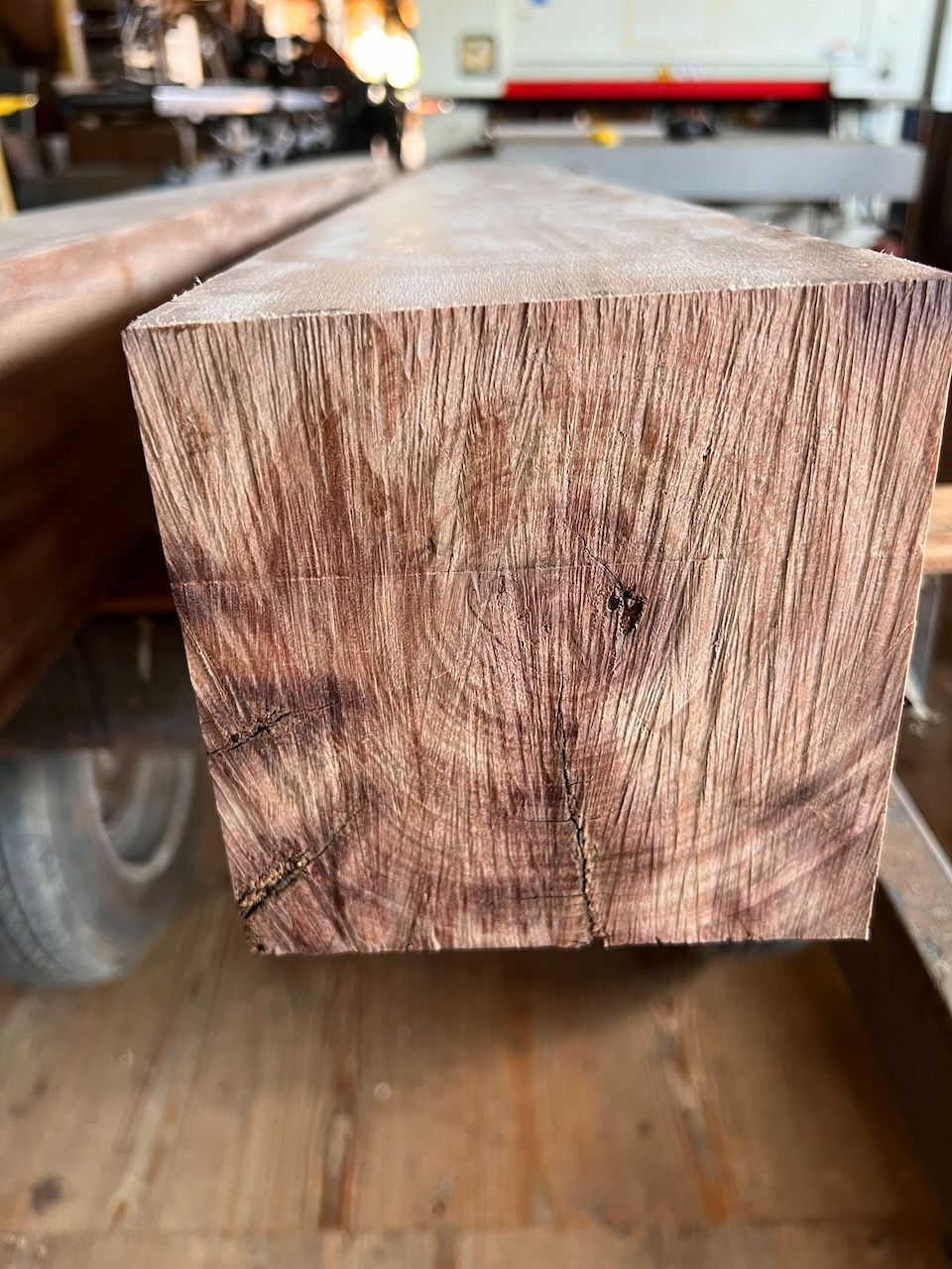 Close-up of a rectangular block of reddish-brown wood, likely lumber, in a workshop setting.