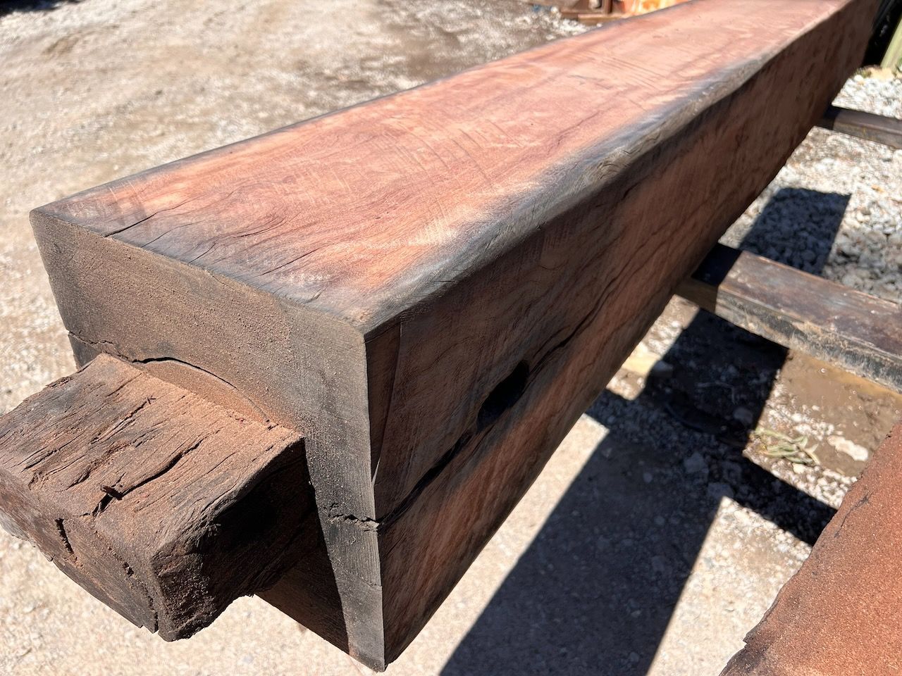 A large, rectangular dark-brown wooden beam with a visible grain, resting on wooden supports in an outdoor setting.