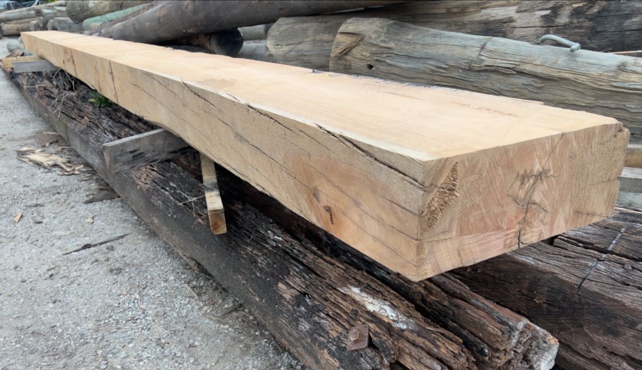 A long, rectangular, light-brown wooden beam rests on weathered, darker-toned wooden beams.