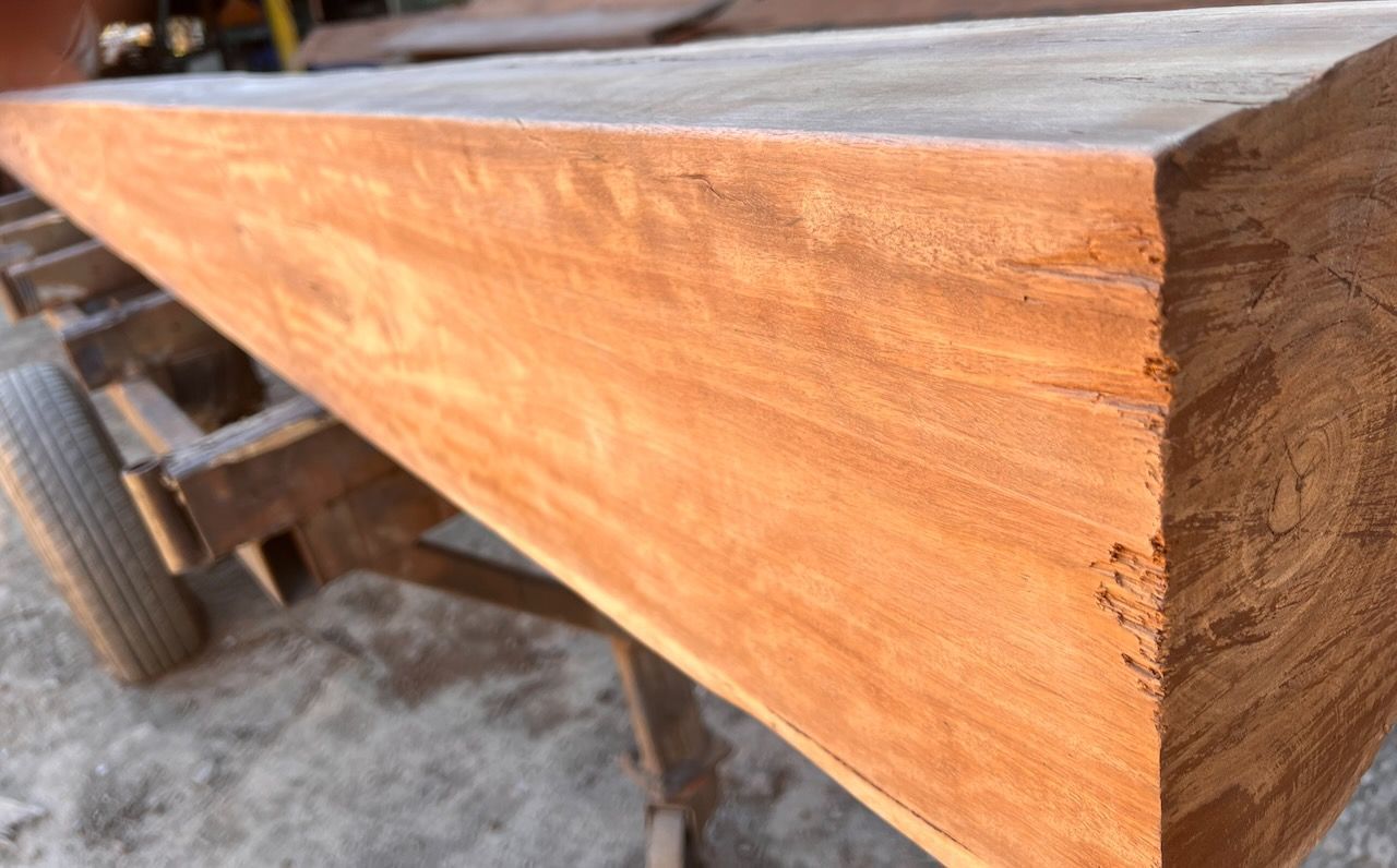 Close-up of a rectangular, light-brown wooden beam on a wheeled cart.