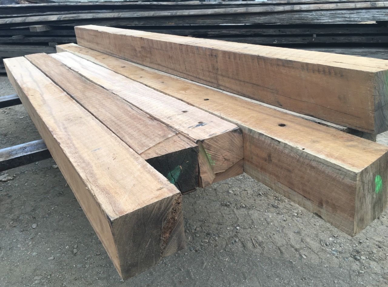 Wooden beams, stacked, varying lengths, light brown color, outdoors, possibly lumberyard.