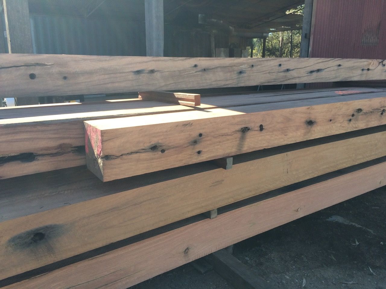 Wooden beams, varying sizes and colors, stacked outdoors on a sunny day.