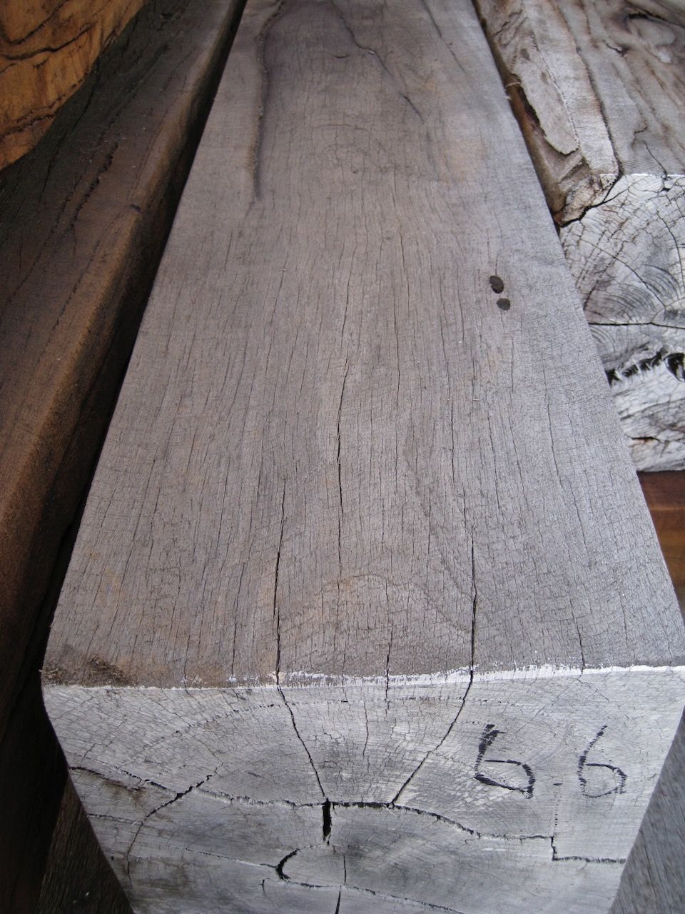 Close-up of a weathered, grey-toned wooden beam with cracks and markings;