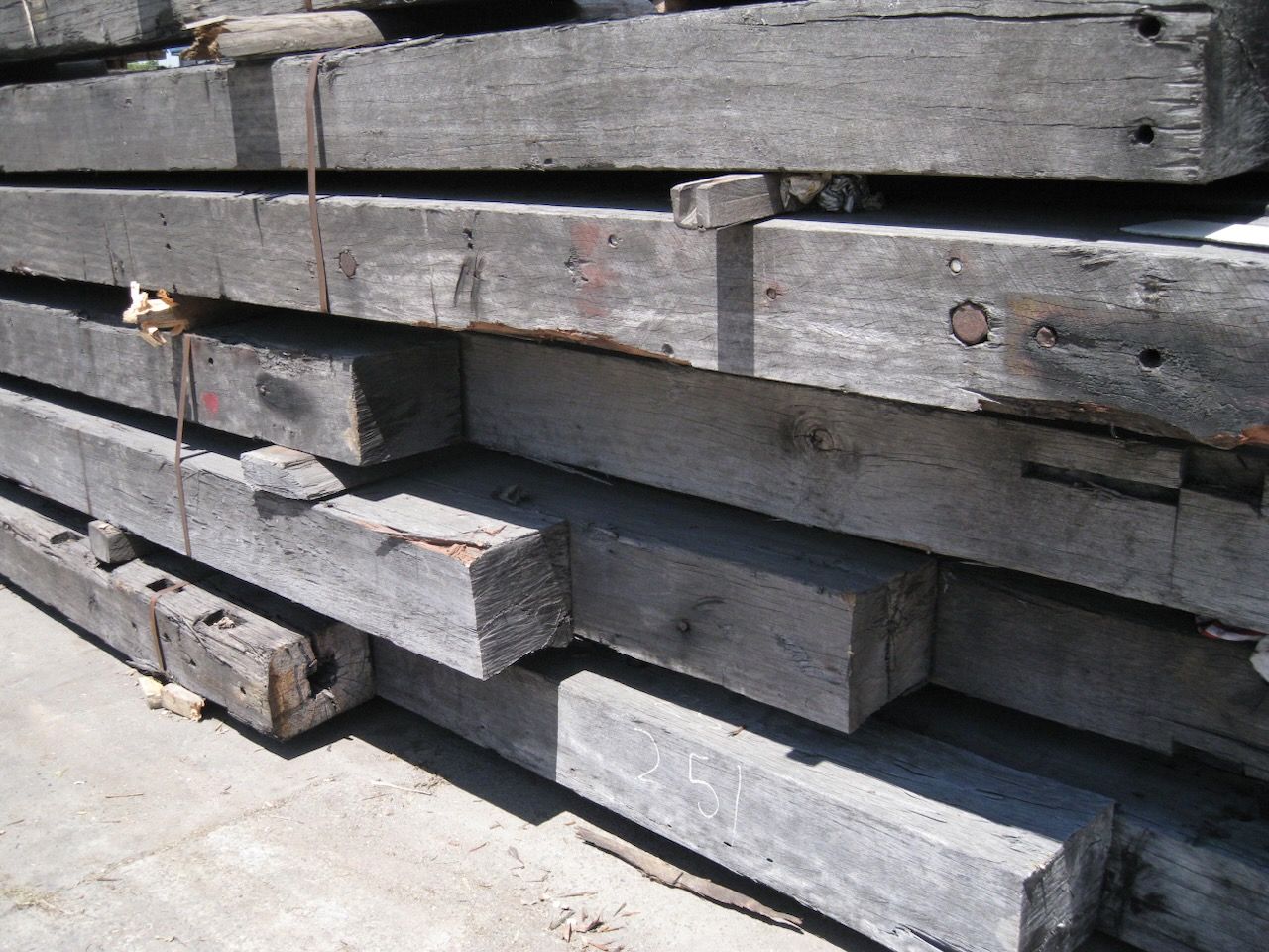 Pile of weathered, gray rectangular wooden beams stacked outdoors.