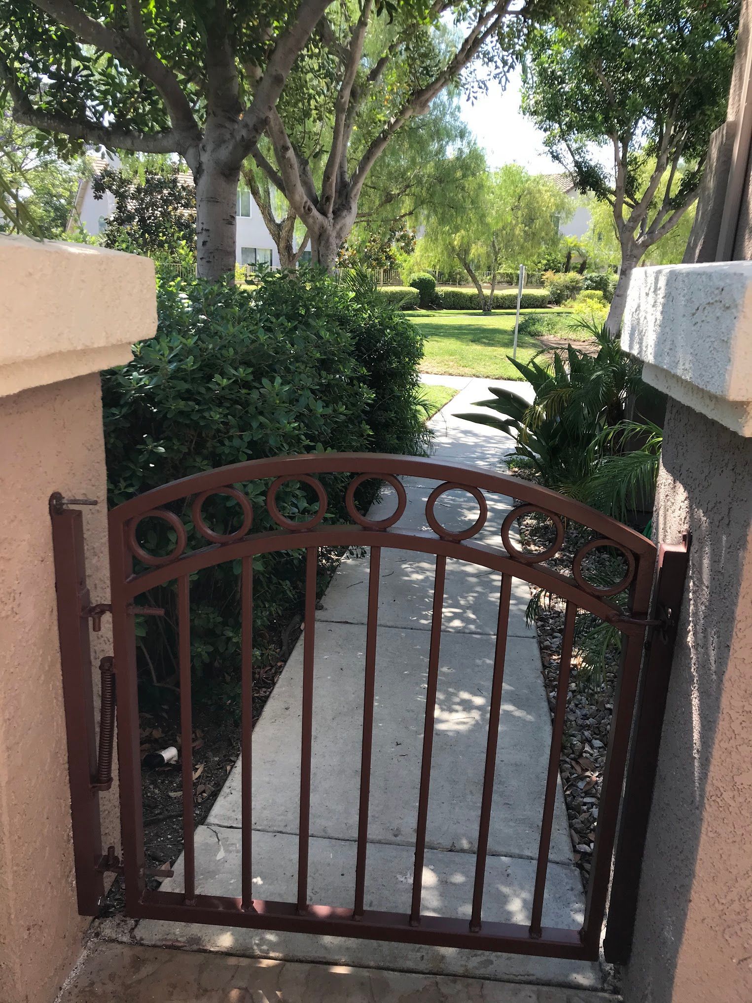 A wrought iron gate leads to a sidewalk and a park.