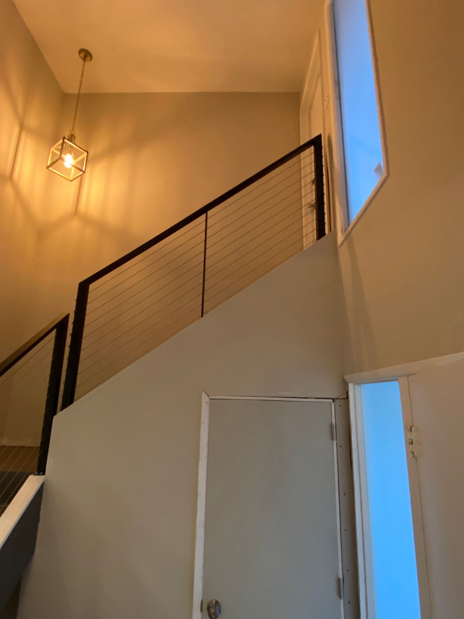 Staircase with black railing and wire cables, leading upwards. Door visible below.