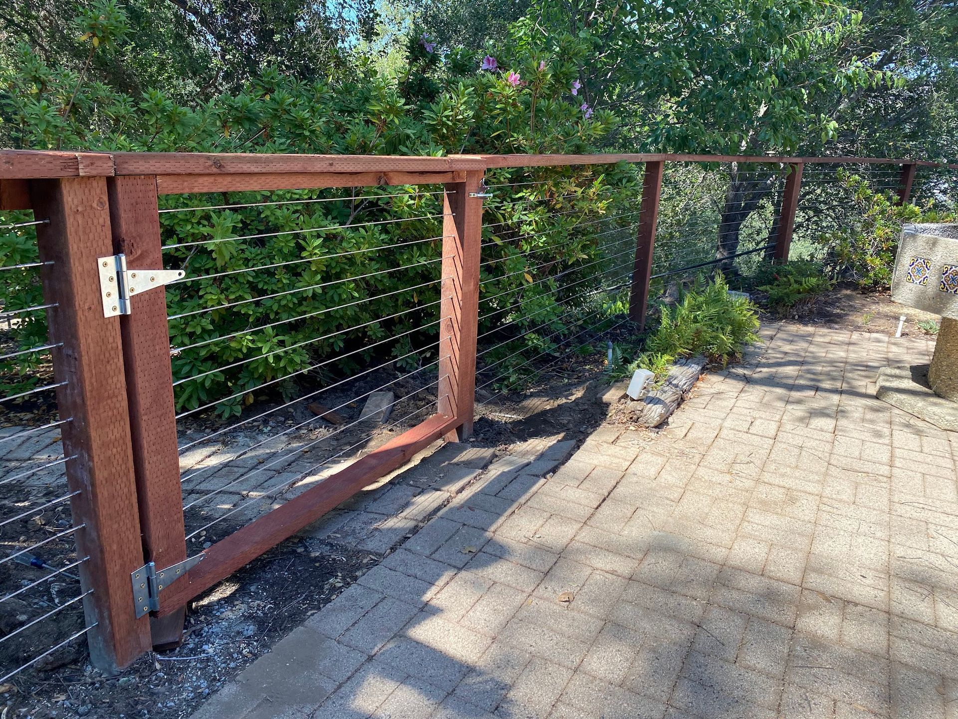 A wooden fence with a gate is surrounded by trees and a brick walkway.