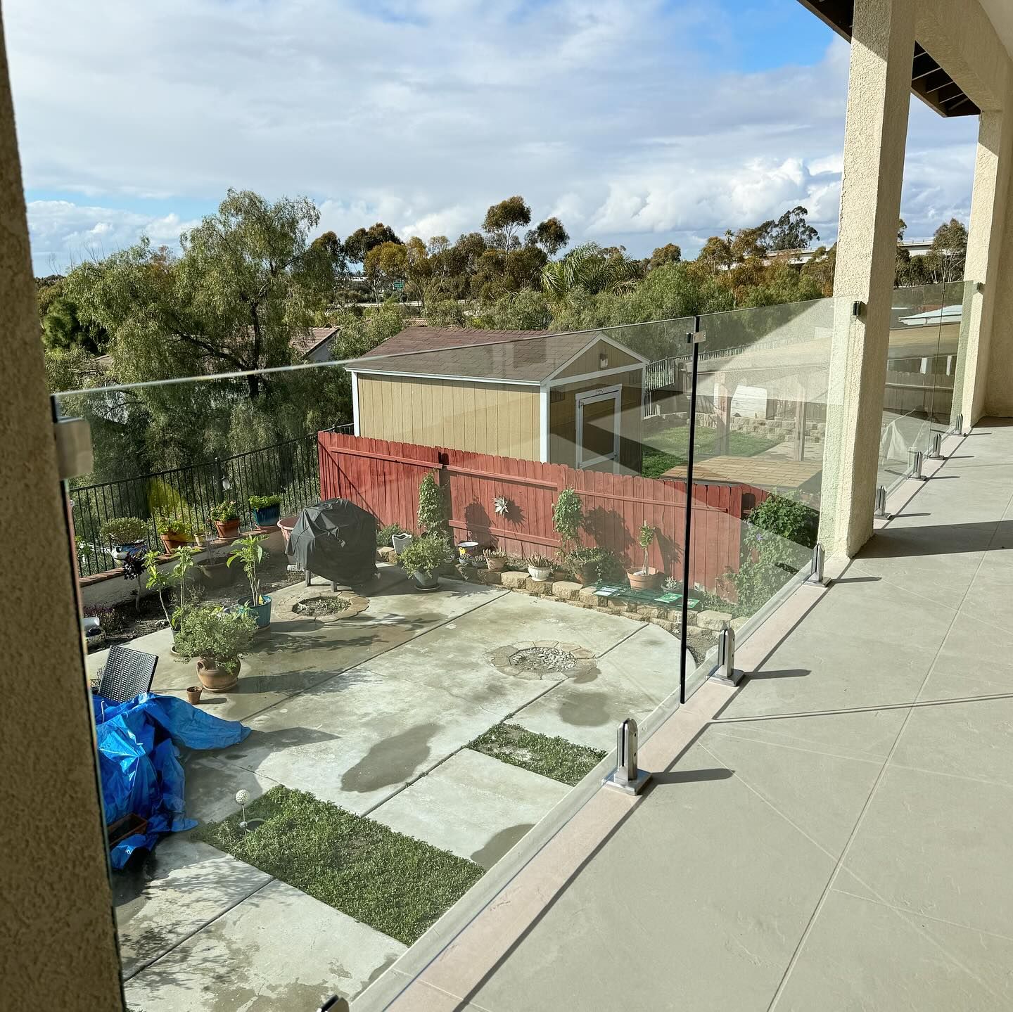 A balcony with a glass railing overlooking a backyard