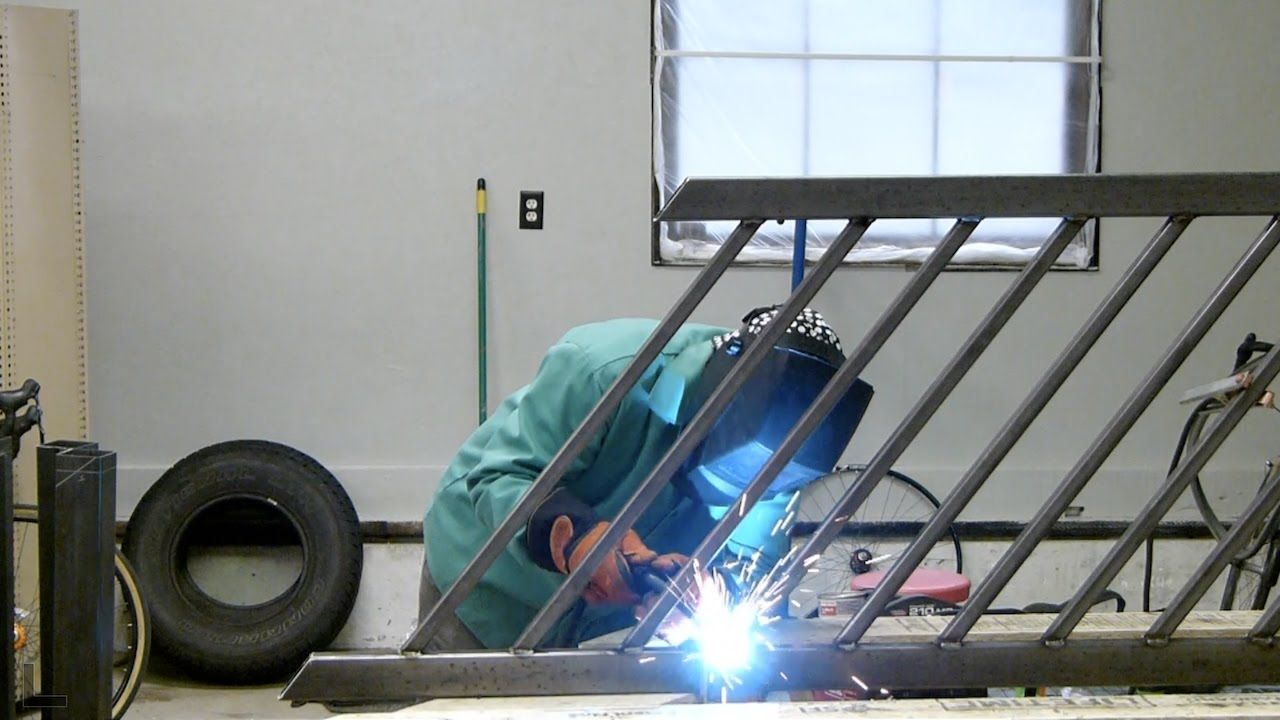 A man wearing a welding mask is welding a metal railing