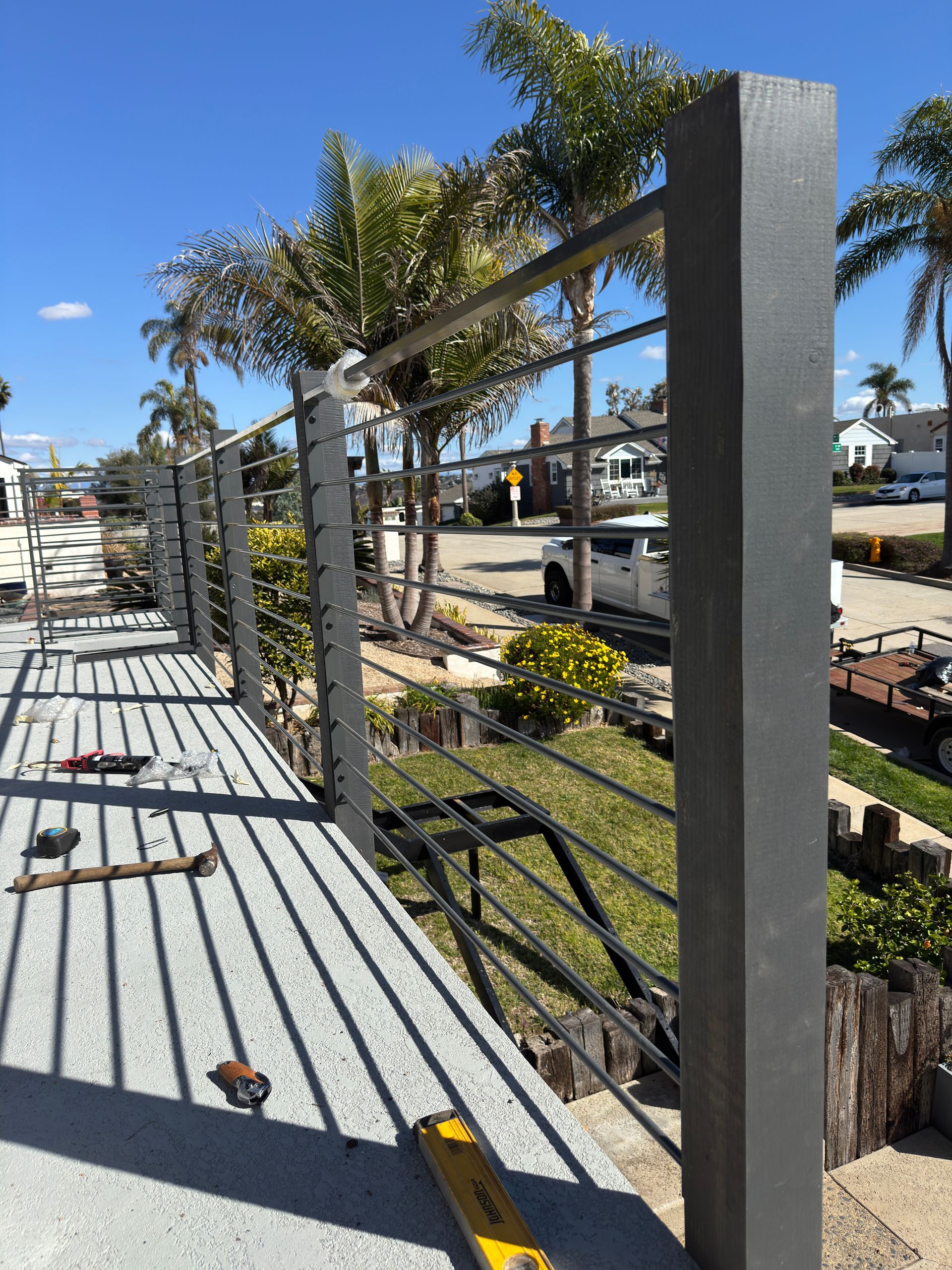 A metal railing is being built on a deck with palm trees in the background