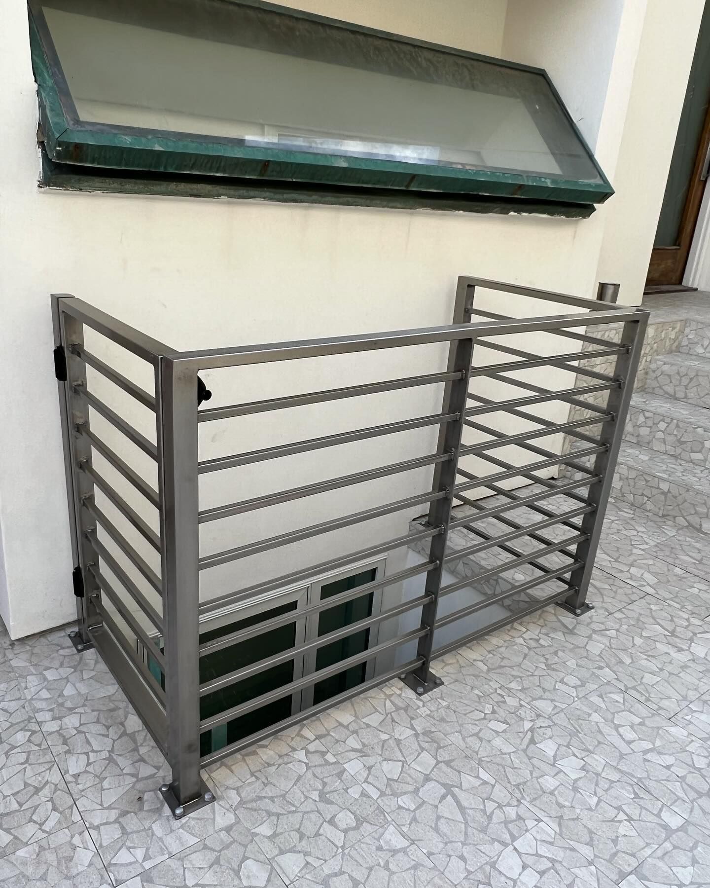 A metal railing is sitting outside of a building next to a window.