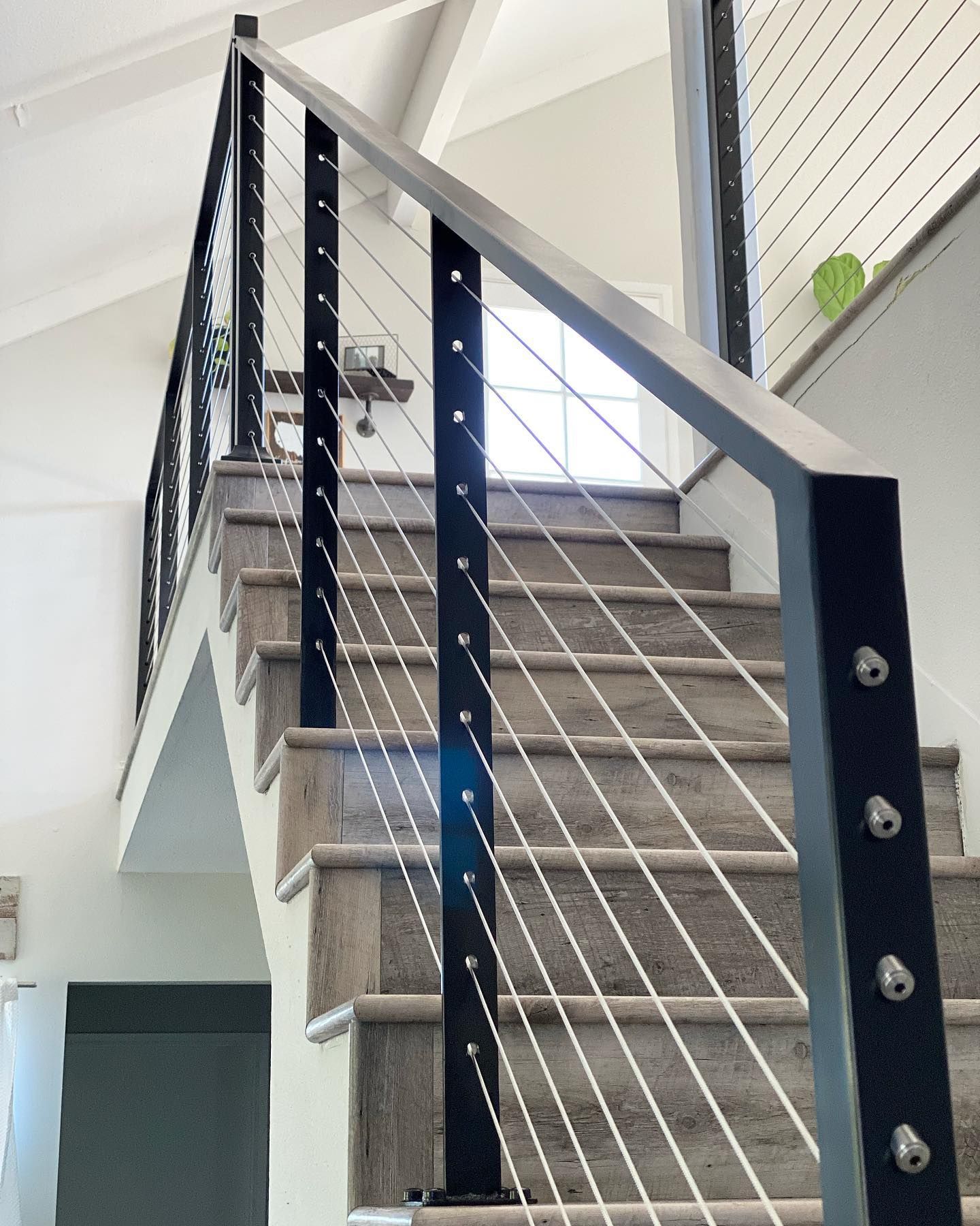 Staircase with gray treads and a black metal railing with stainless steel cable.
