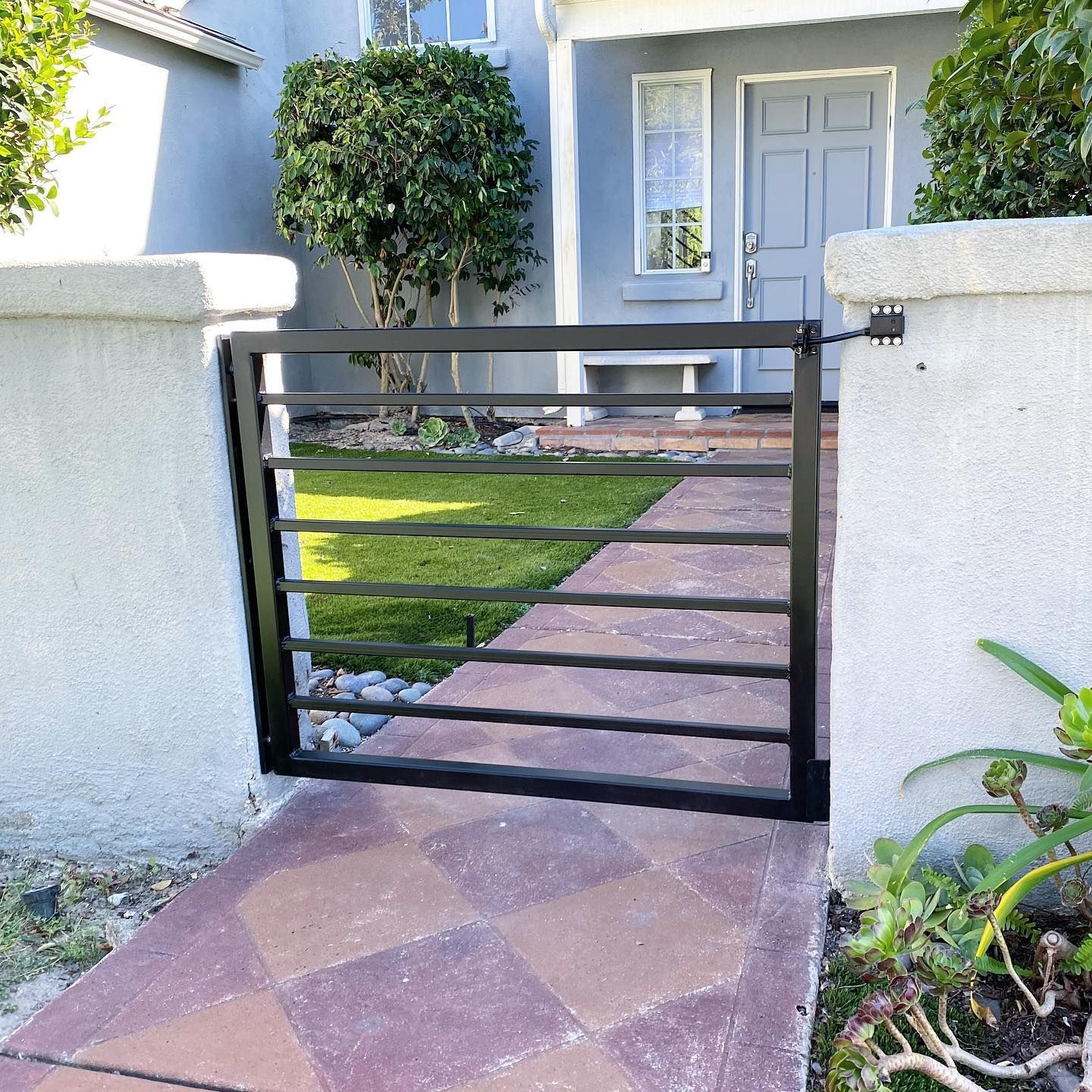 A black gate is open to a walkway leading to a house