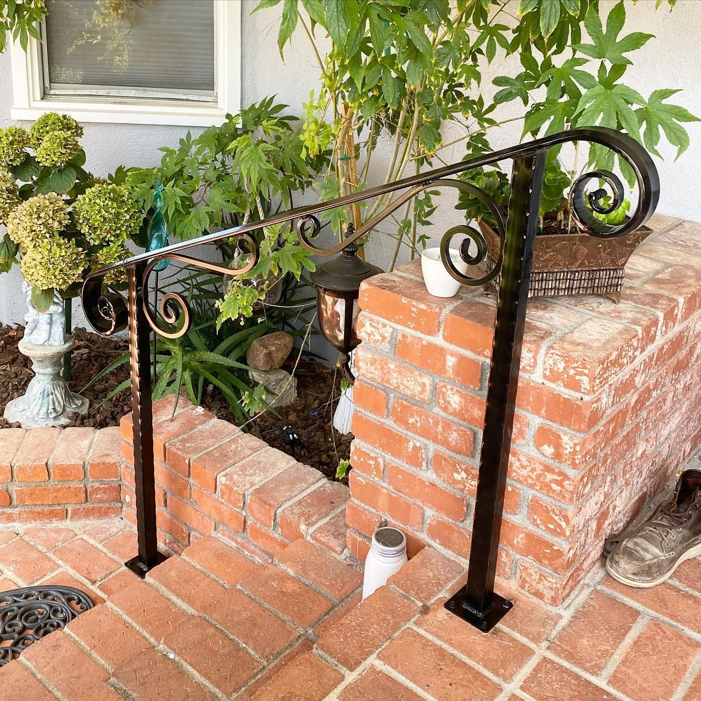 A black railing is sitting on a brick porch next to a brick wall.