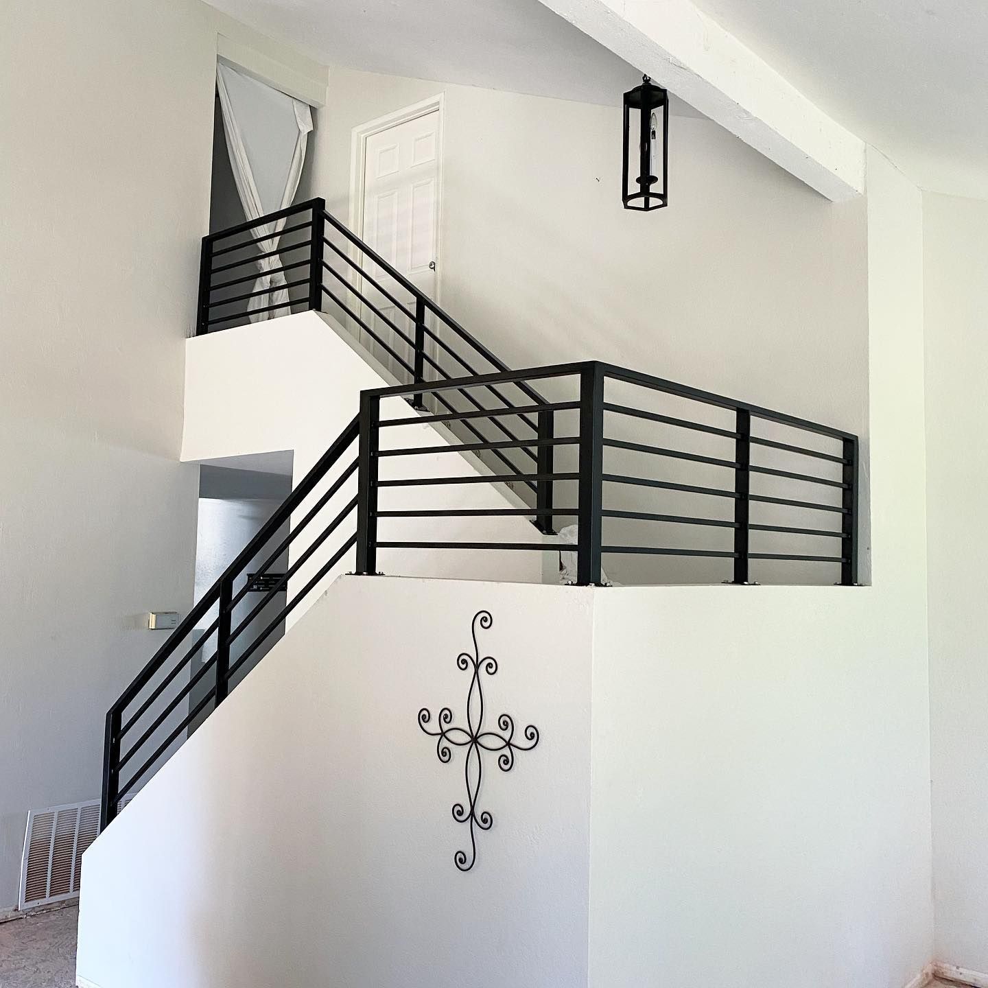 A staircase with a black railing and a cross on the wall