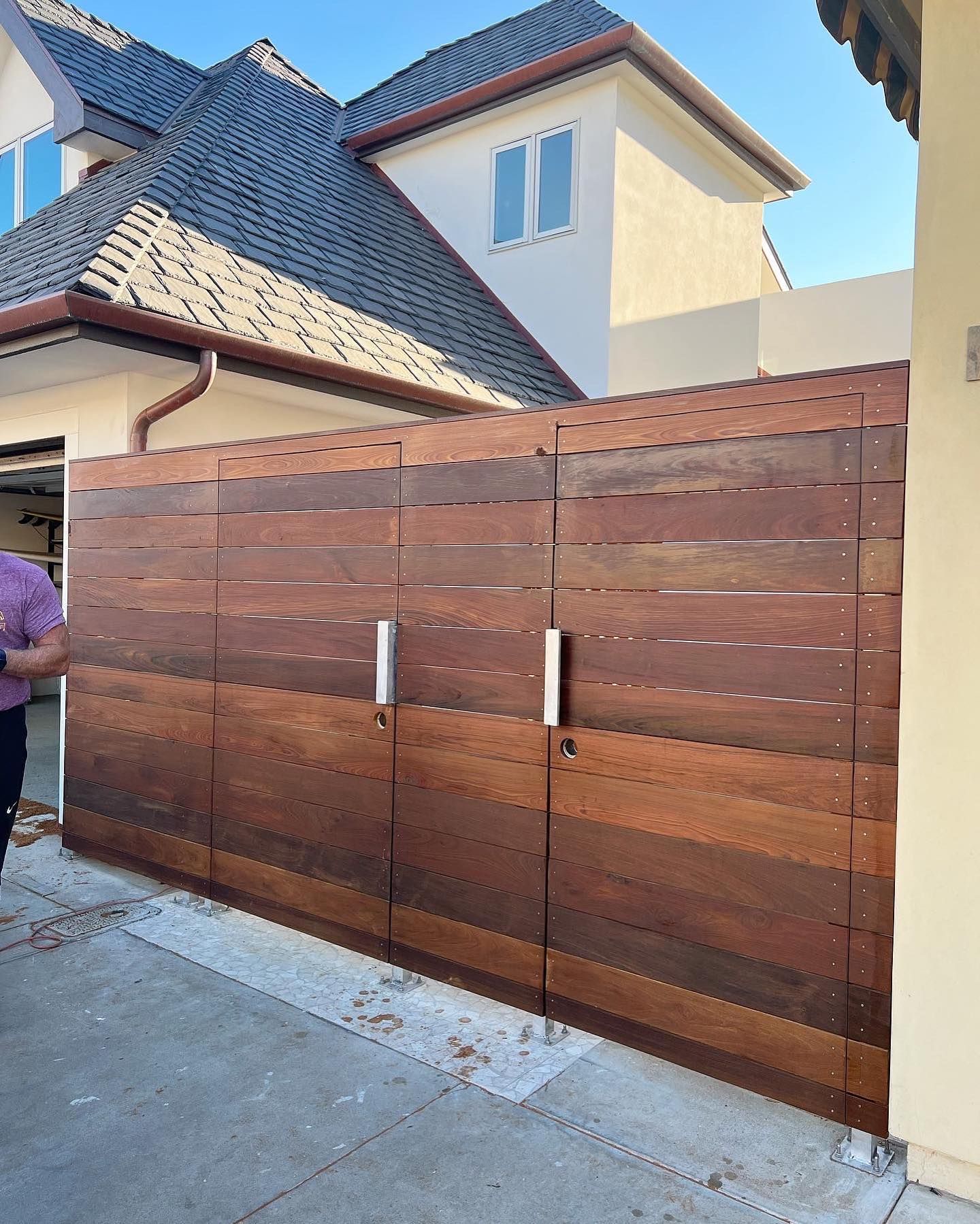 A man is standing next to a wooden fence in front of a house.