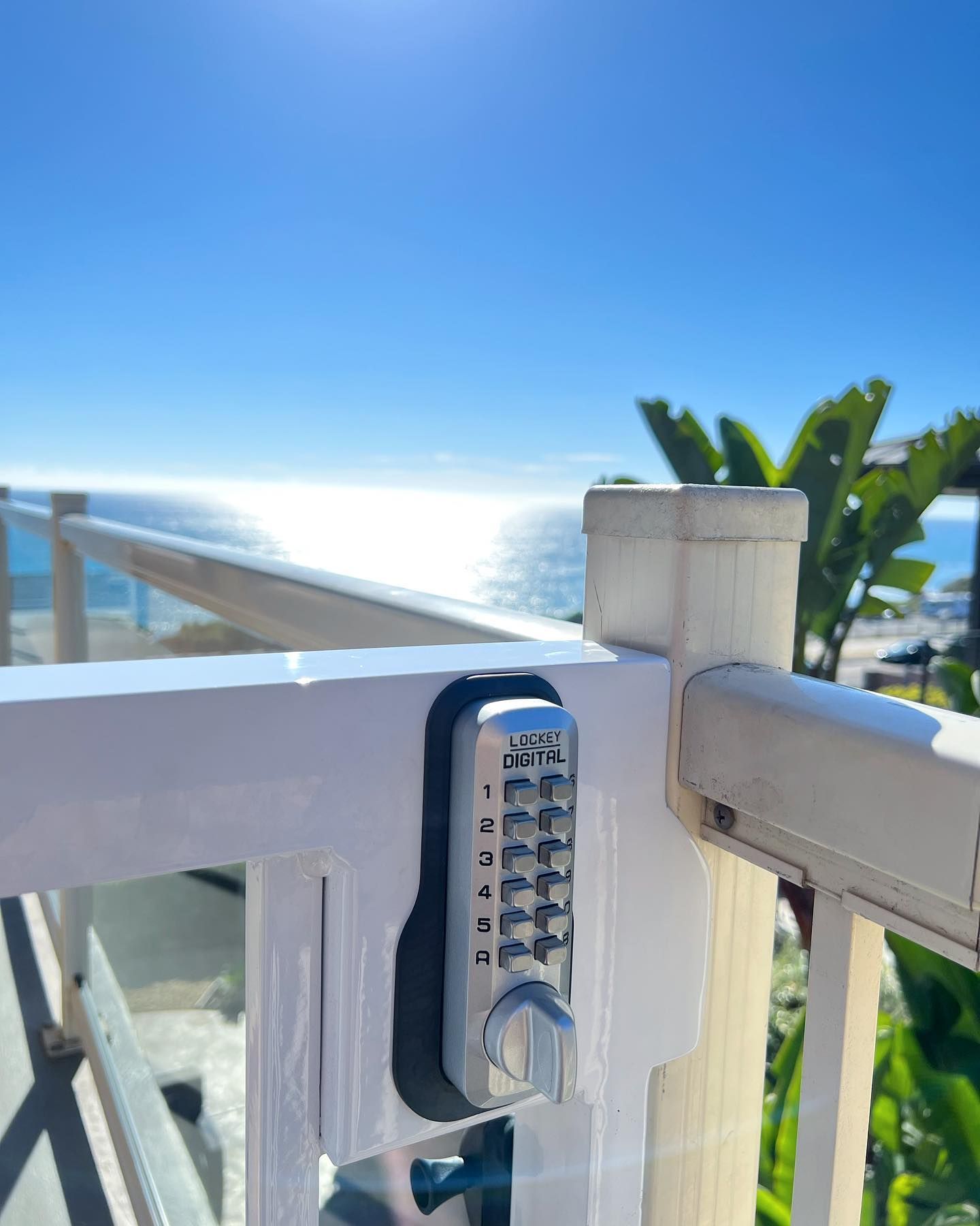 A close up of a combination lock on a railing overlooking the ocean.
