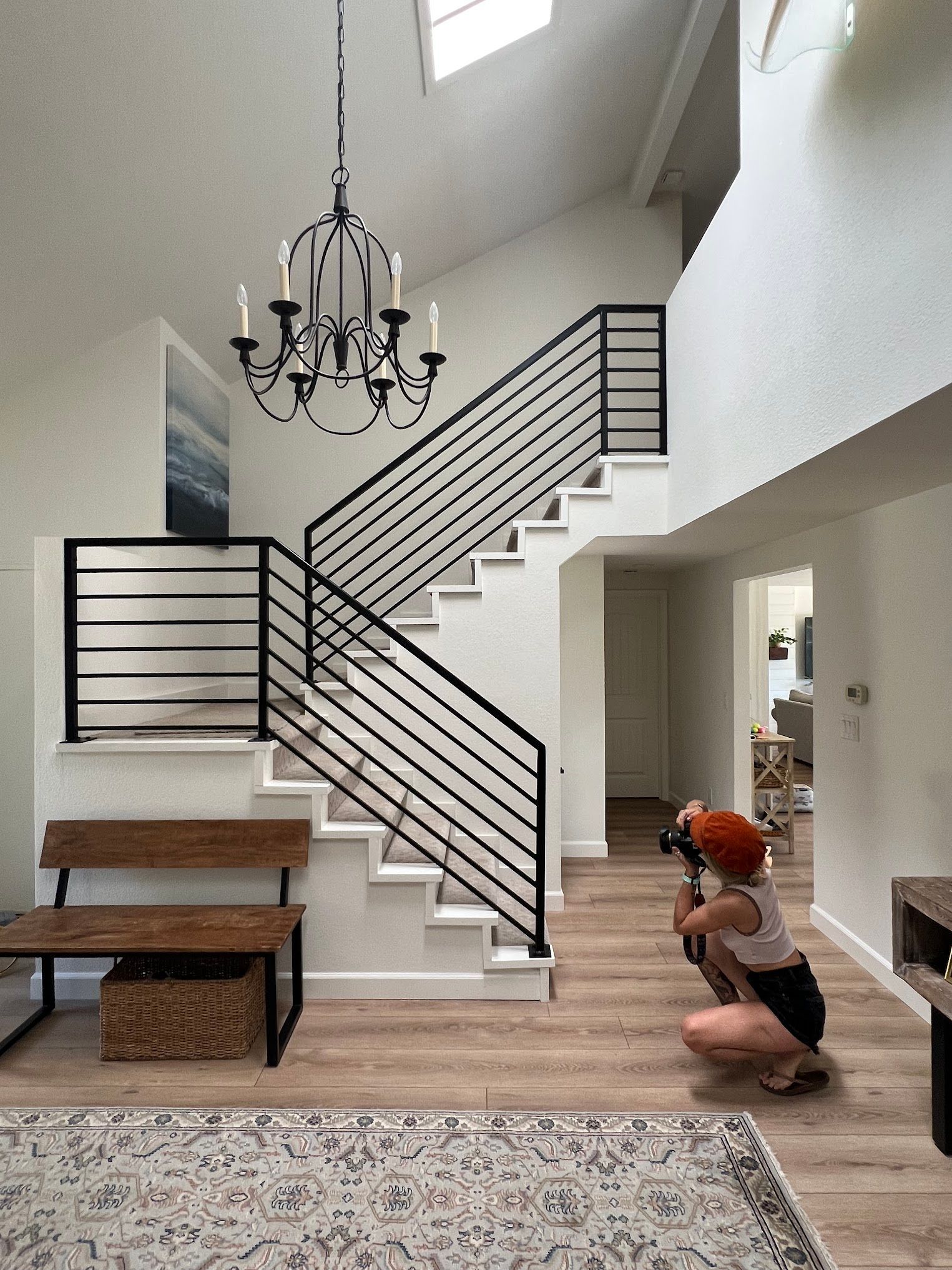 A woman is kneeling down in front of a staircase in a living room.