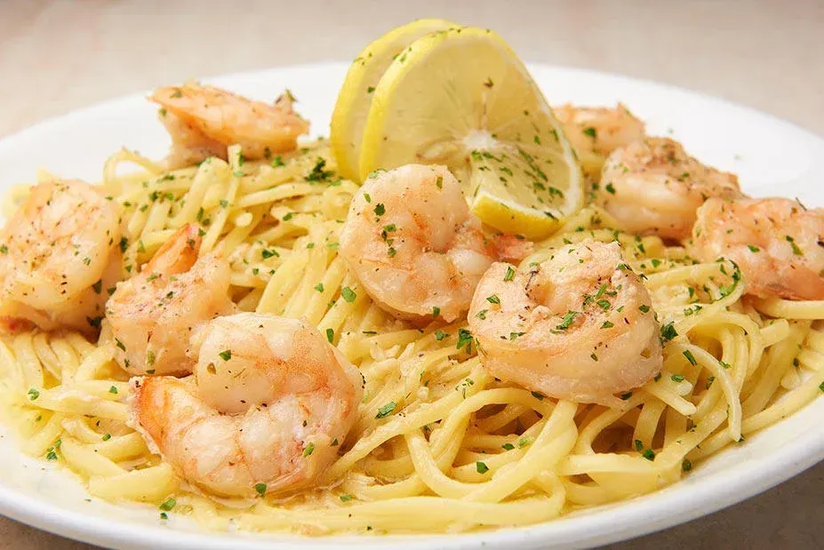 Shrimp scampi served over pasta, garnished with lemon and parsley.