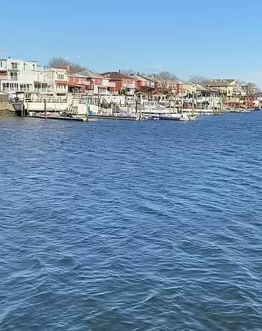 Waterfront houses with docks and boats along a blue body of water on a sunny day.