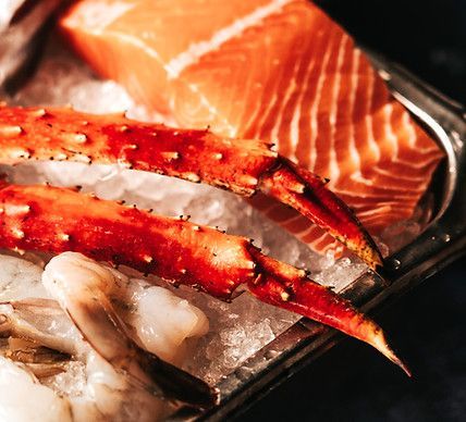 Crab legs, salmon, and shrimp on ice in a silver tray.