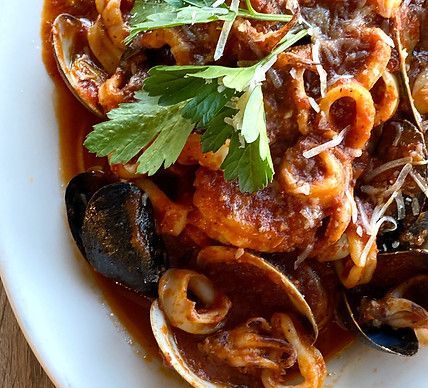 Seafood stew with clams, mussels, and calamari in a red sauce, garnished with parsley.