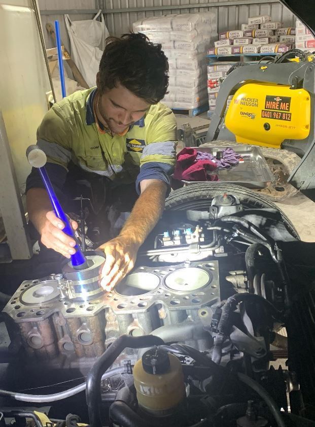 A man is working on a car engine with a flashlight.