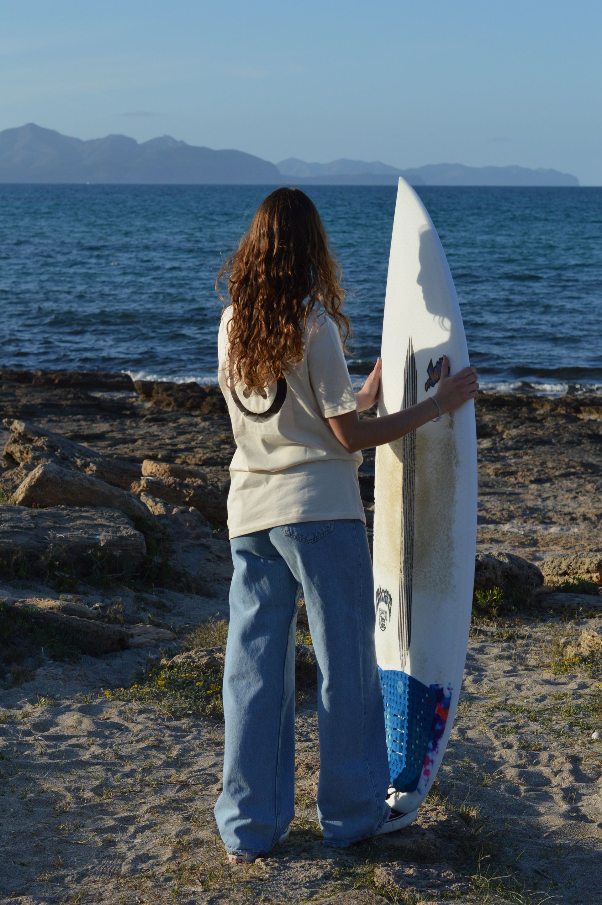 Una mujer sostiene una tabla de surf frente al océano.