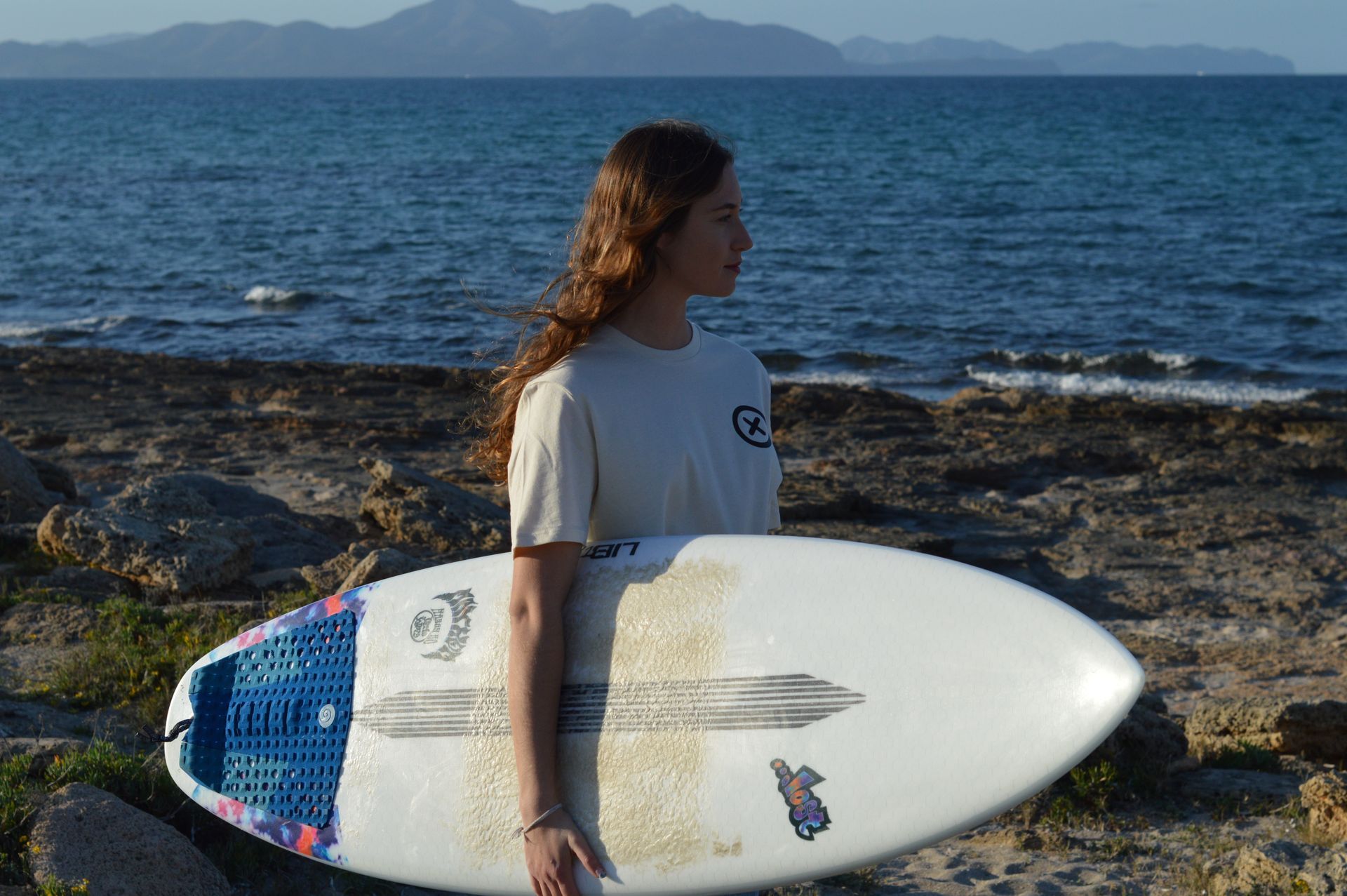 Una mujer sostiene una tabla de surf frente al océano.