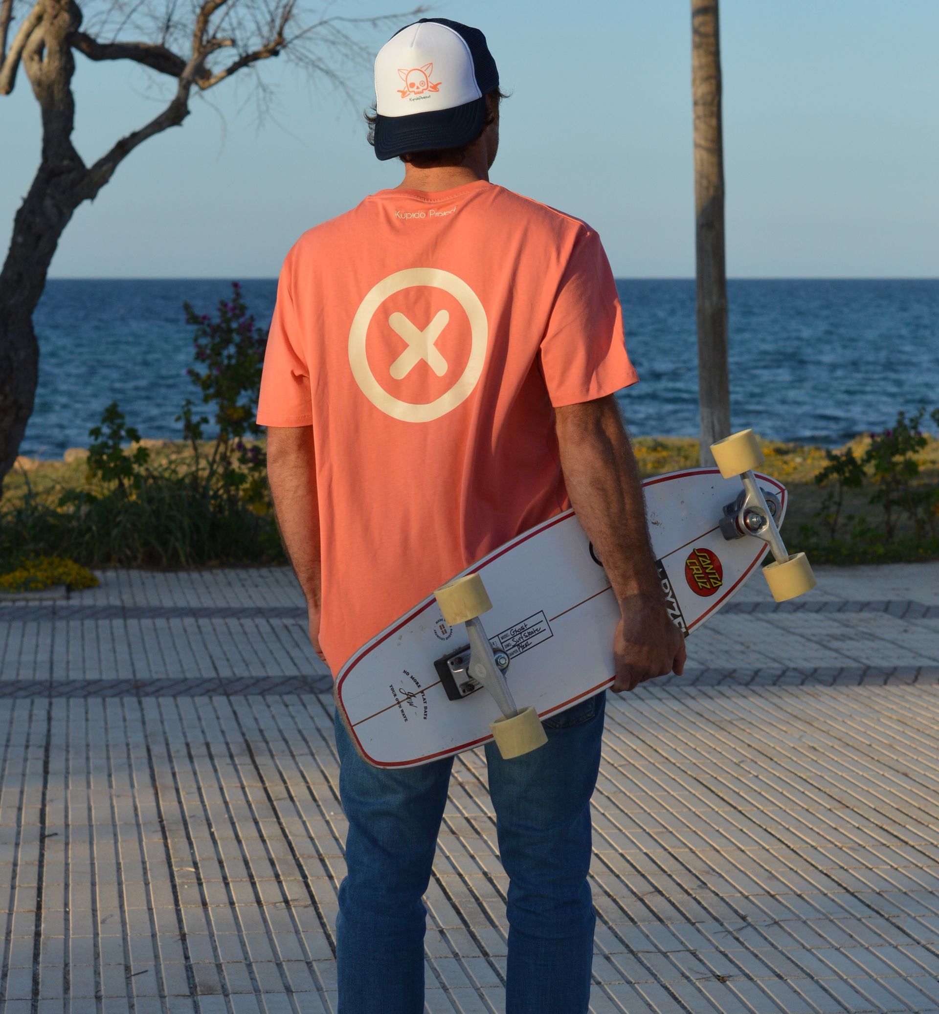 Un hombre con una camisa roja con una x en la espalda sostiene un skate.