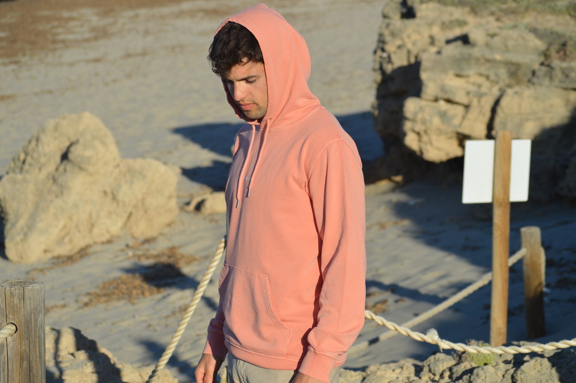 Un hombre que lleva una sudadera con capucha rosa está parado en una playa.
